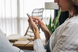 Closeup of Young Woman Sitting on Sofa and Using Touch Screen on Cellphone