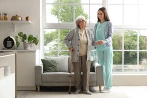 Young,Caregiver,Helping,Senior,Woman,With,Stick,To,Walk,In